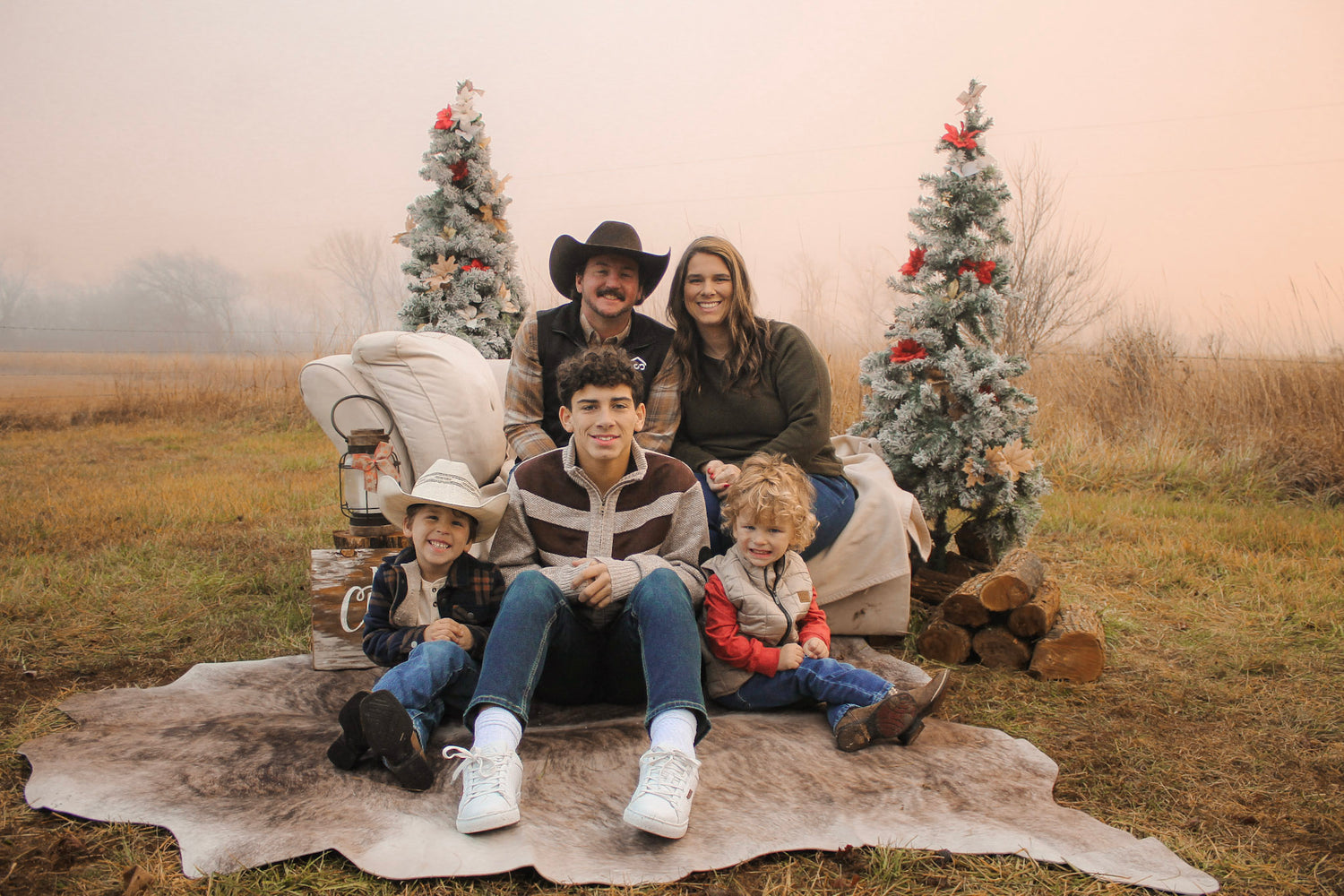 Family of five posing outdoors with Christmas trees in a field.